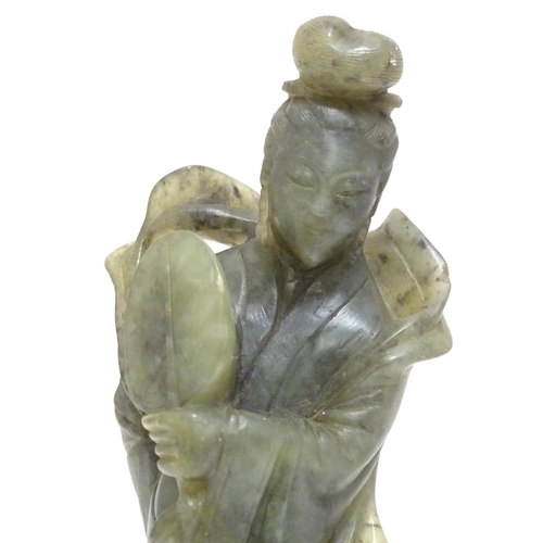 867 - An Oriental carved soapstone figure of a lady holding a fan, wearing flowing robes, on a carved base... 