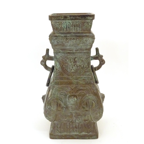 876 - An Oriental cast bronze vase with twin mask handles with a looped ring, the body decorated with styl... 