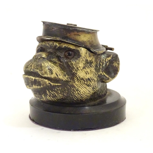 907 - A Victorian novelty brass desk inkwell formed as the head of a monkey with glass eyes wearing a hat.... 