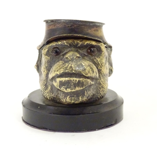 907 - A Victorian novelty brass desk inkwell formed as the head of a monkey with glass eyes wearing a hat.... 