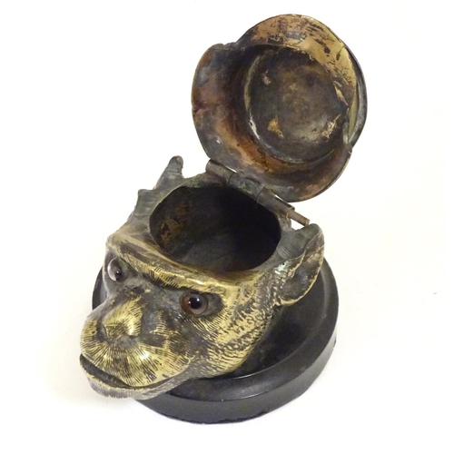 907 - A Victorian novelty brass desk inkwell formed as the head of a monkey with glass eyes wearing a hat.... 