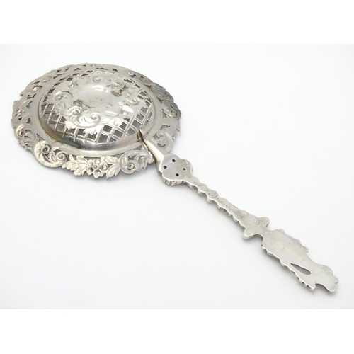 348 - An ornate silver strainer / sifter spoon with figural detail to handle and floral and acanthus detai... 