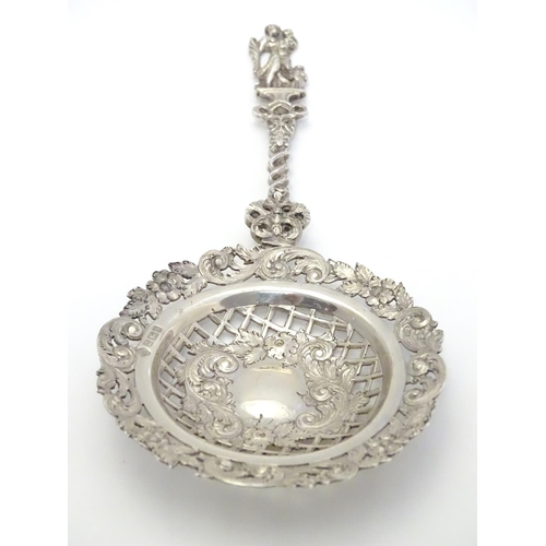 348 - An ornate silver strainer / sifter spoon with figural detail to handle and floral and acanthus detai... 