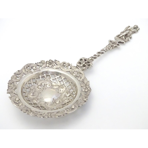 348 - An ornate silver strainer / sifter spoon with figural detail to handle and floral and acanthus detai... 