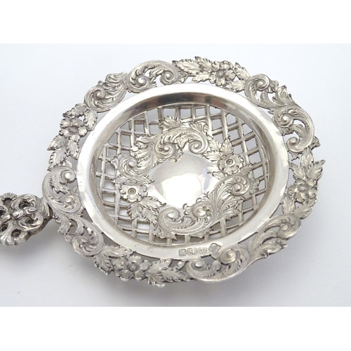 348 - An ornate silver strainer / sifter spoon with figural detail to handle and floral and acanthus detai... 