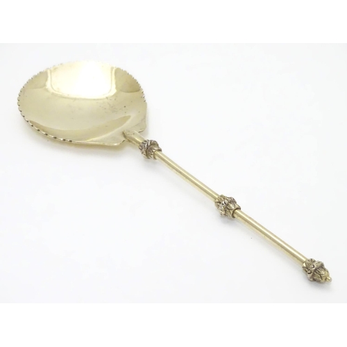 406 - An unusual silver gilt serving spoon, the bowl having rounded serrated edge, the stem and terminal h... 