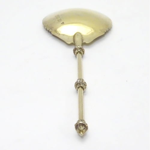 406 - An unusual silver gilt serving spoon, the bowl having rounded serrated edge, the stem and terminal h... 