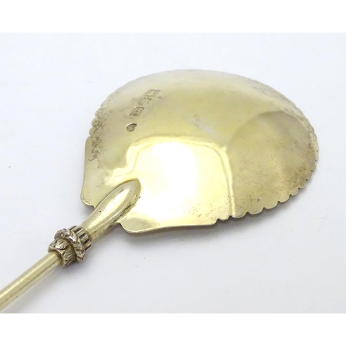 406 - An unusual silver gilt serving spoon, the bowl having rounded serrated edge, the stem and terminal h... 