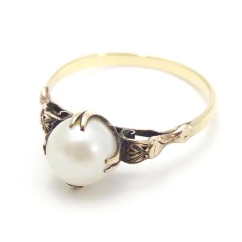 441 - A yellow metal ring with claw set pearl and decorative shoulders. Ring size approx O