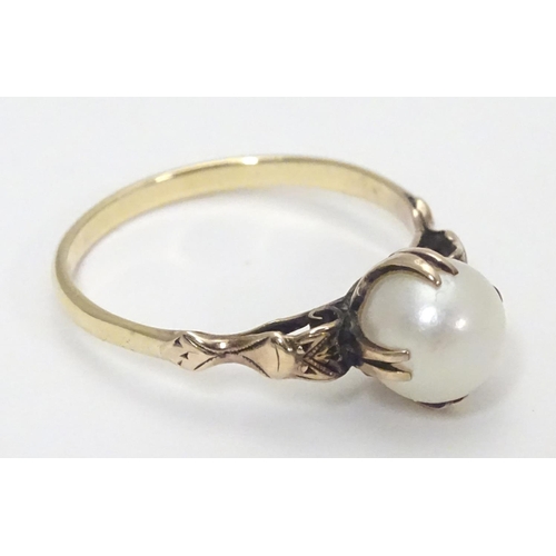 441 - A yellow metal ring with claw set pearl and decorative shoulders. Ring size approx O