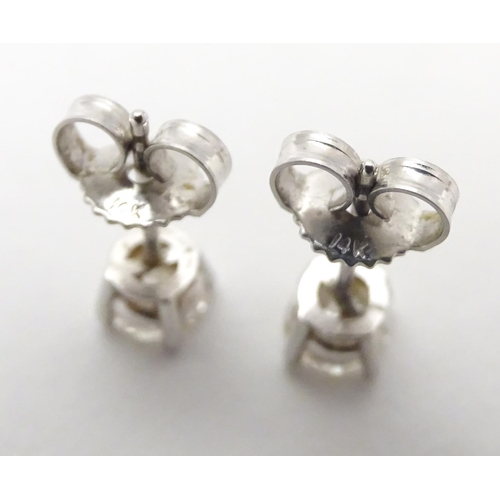 483 - A pair of white gold stud earrings set with diamond solitaires. The diamond approximately 1/8