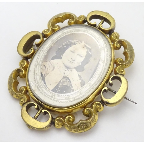 503 - A Victorian gilt metal brooch of locket form with glazed font and back central section within a C-sc... 