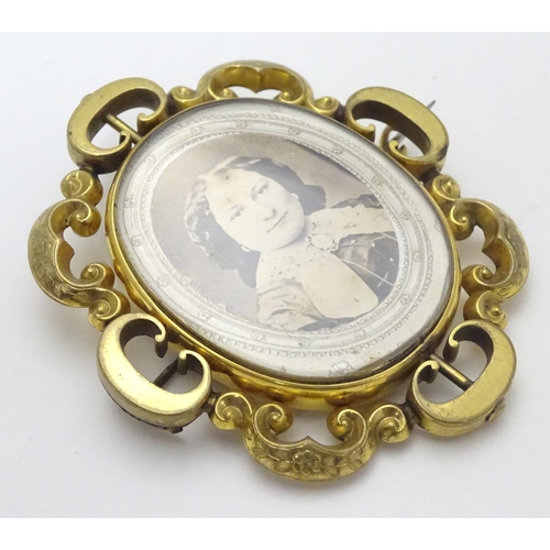 503 - A Victorian gilt metal brooch of locket form with glazed font and back central section within a C-sc... 