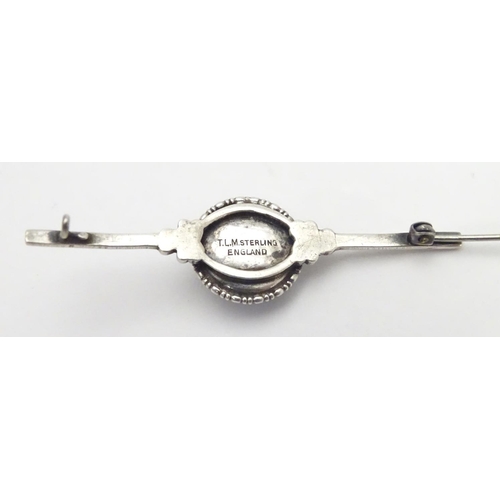 505 - A silver bar brooch, the central circular section mounted with butterfly wing detail behind glass. M... 