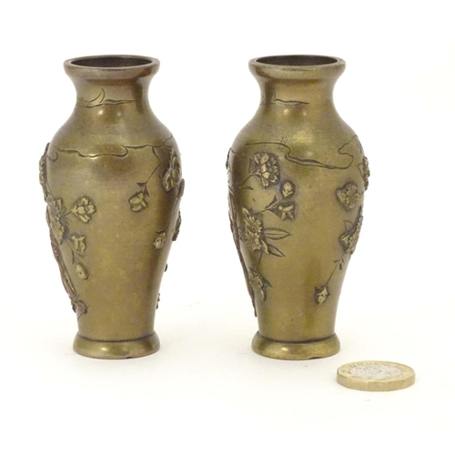 832 - A pair of late 19th / early 20thC miniature brass vases with engraved and relief decoration depictin... 