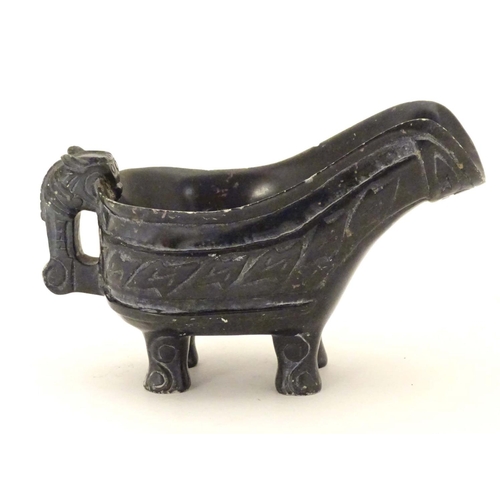 839 - An Oriental carved stone vessel with a pouring spout, beast formed handle and four feet. The side in... 