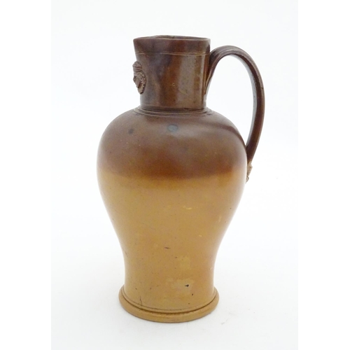 116 - A Doulton Lambeth two tone stoneware jug with relief mask detail to neck. Impressed marks under. App... 