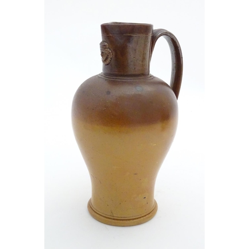 116 - A Doulton Lambeth two tone stoneware jug with relief mask detail to neck. Impressed marks under. App... 