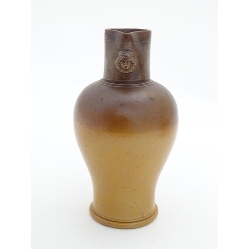 116 - A Doulton Lambeth two tone stoneware jug with relief mask detail to neck. Impressed marks under. App... 