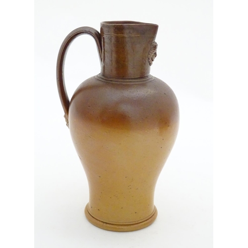 116 - A Doulton Lambeth two tone stoneware jug with relief mask detail to neck. Impressed marks under. App... 