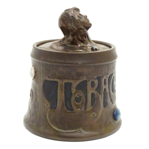 74 - A Bretby Art Nouveau tobacco pot with faux hammered copper effect and enamelled cabochon detail. The... 