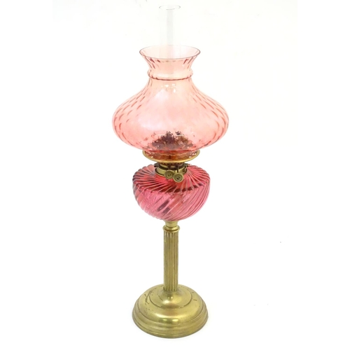 1526 - A Victorian oil lamp, the brass column with cranberry glass reservoir and shade. The twin burners ma... 