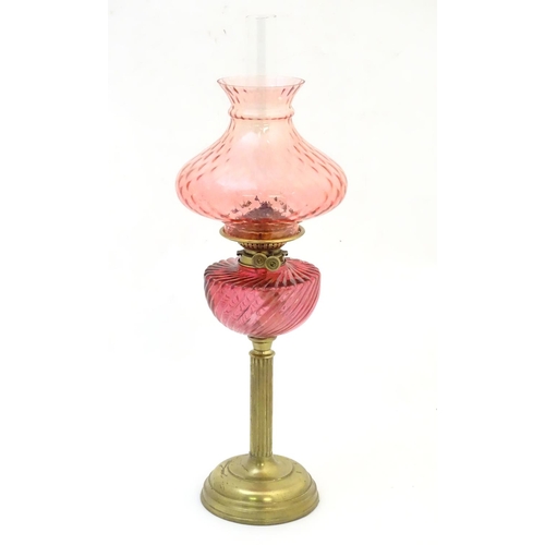 1526 - A Victorian oil lamp, the brass column with cranberry glass reservoir and shade. The twin burners ma... 