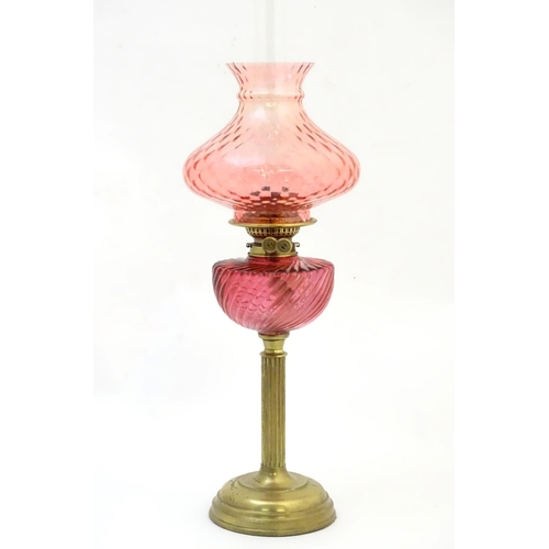 1526 - A Victorian oil lamp, the brass column with cranberry glass reservoir and shade. The twin burners ma... 