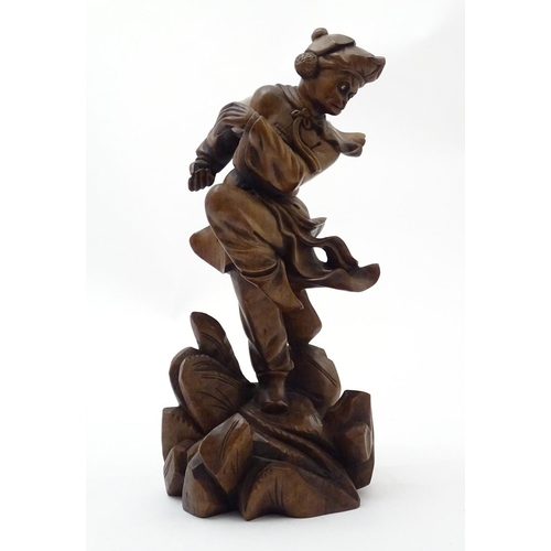 849 - An Oriental carved wooden figure modelled as man on a rocky outcrop with foliate detail. Approx. 12 ... 