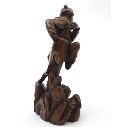 849 - An Oriental carved wooden figure modelled as man on a rocky outcrop with foliate detail. Approx. 12 ... 