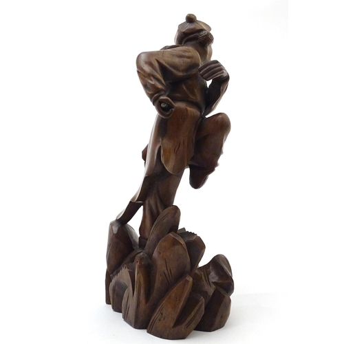 849 - An Oriental carved wooden figure modelled as man on a rocky outcrop with foliate detail. Approx. 12 ... 