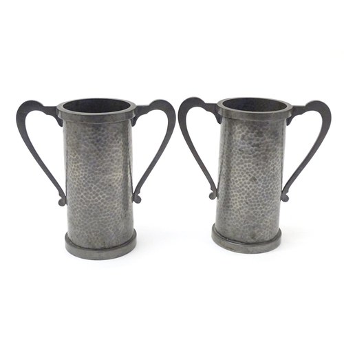 817 - A pair of Arts & Crafts pewter vases of cylindrical form with twin handles and hammered decoration b... 