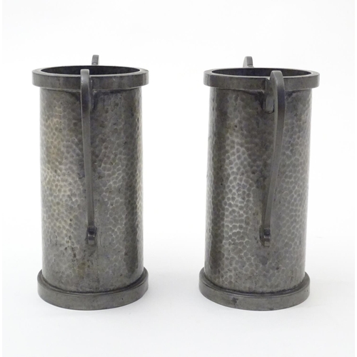 817 - A pair of Arts & Crafts pewter vases of cylindrical form with twin handles and hammered decoration b... 