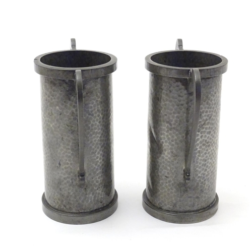 817 - A pair of Arts & Crafts pewter vases of cylindrical form with twin handles and hammered decoration b... 