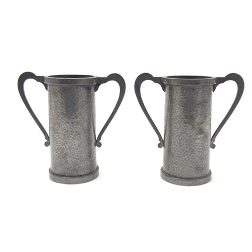 817 - A pair of Arts & Crafts pewter vases of cylindrical form with twin handles and hammered decoration b... 