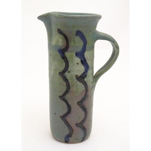 99 - A studio pottery jug of cylindrical form with a green ground and blue detail. Impressed maker's mark... 