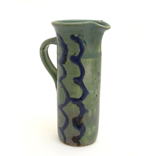 99 - A studio pottery jug of cylindrical form with a green ground and blue detail. Impressed maker's mark... 