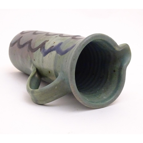 99 - A studio pottery jug of cylindrical form with a green ground and blue detail. Impressed maker's mark... 