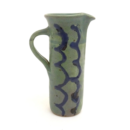 99 - A studio pottery jug of cylindrical form with a green ground and blue detail. Impressed maker's mark... 