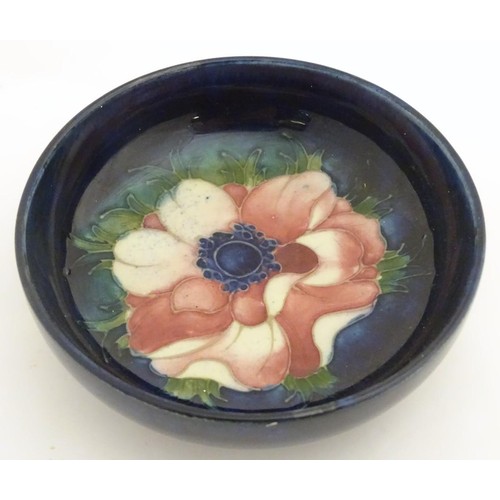 131 - A 20thC Moorcroft circular dish decorated with an anemone flower on a blue ground. Marked under. App... 