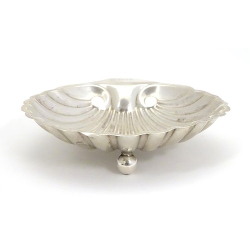 236 - A silver scallop-shaped dish raised on three bun feet. Hallmarked Sheffield 1910 maker Harrison Brot... 