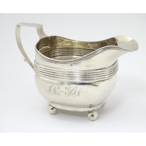 240 - A George III silver cream / milk jug with banded decoration raised on four spherical feet. Hallmarke... 