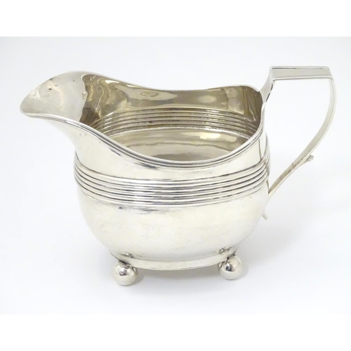 240 - A George III silver cream / milk jug with banded decoration raised on four spherical feet. Hallmarke... 