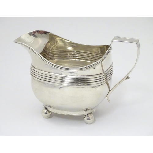 240 - A George III silver cream / milk jug with banded decoration raised on four spherical feet. Hallmarke... 