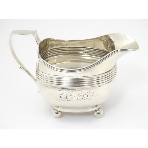 240 - A George III silver cream / milk jug with banded decoration raised on four spherical feet. Hallmarke... 