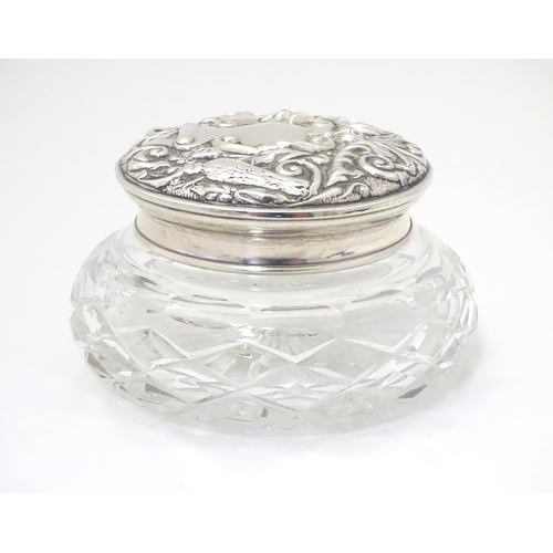 249 - A cut glass powder jar with embossed silver lid, hallmarked Birmingham 1976 maker W I Broadway & Co ... 