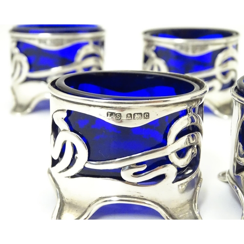 272 - An Art Nouveau silver cruet set comprising four salts and a pepper with blue glass liners and scroll... 