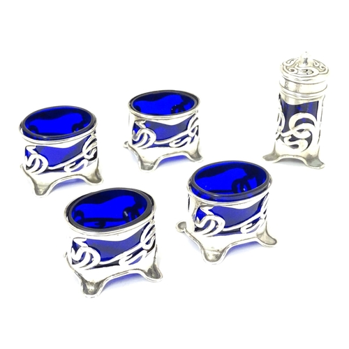 272 - An Art Nouveau silver cruet set comprising four salts and a pepper with blue glass liners and scroll... 