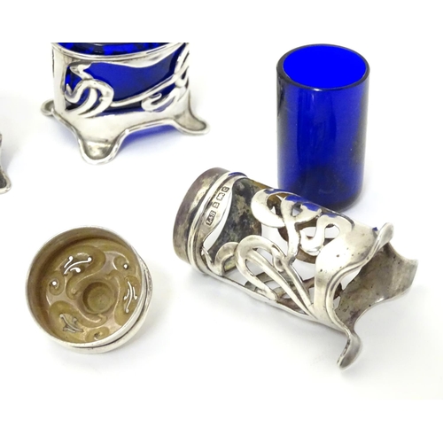 272 - An Art Nouveau silver cruet set comprising four salts and a pepper with blue glass liners and scroll... 