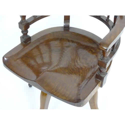 1395 - An early 20thC oak desk chair with a bowed backrest and turned spindle supports above a saddle seat ... 